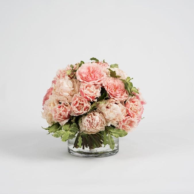 A rounded arrangement of pink flowers and greenery in a glass vase from Tulipanna.